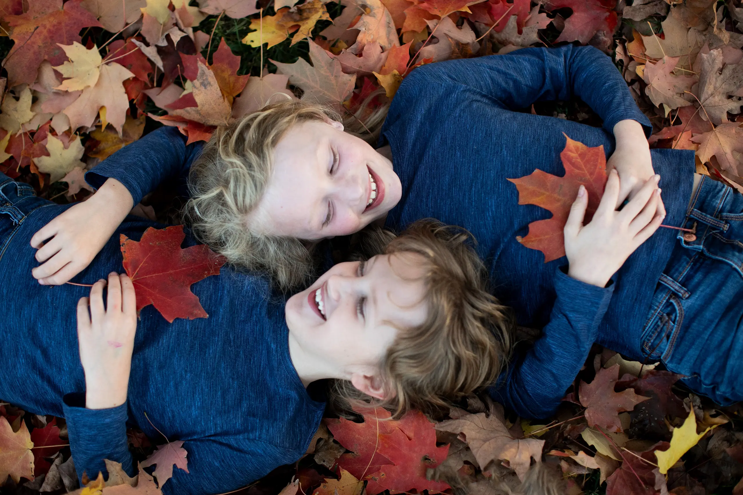 Two girls playing in fallen leaves in autumn